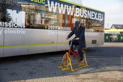 Prezes MPK Janusz Nowakowski na rowerze ze starym wynalazkiem, dynamem do produkcji prądu, na tle autobusu elektrycznego. Łomża podpisała umowę na zakup pierwszych dwóch takich pojazdów.